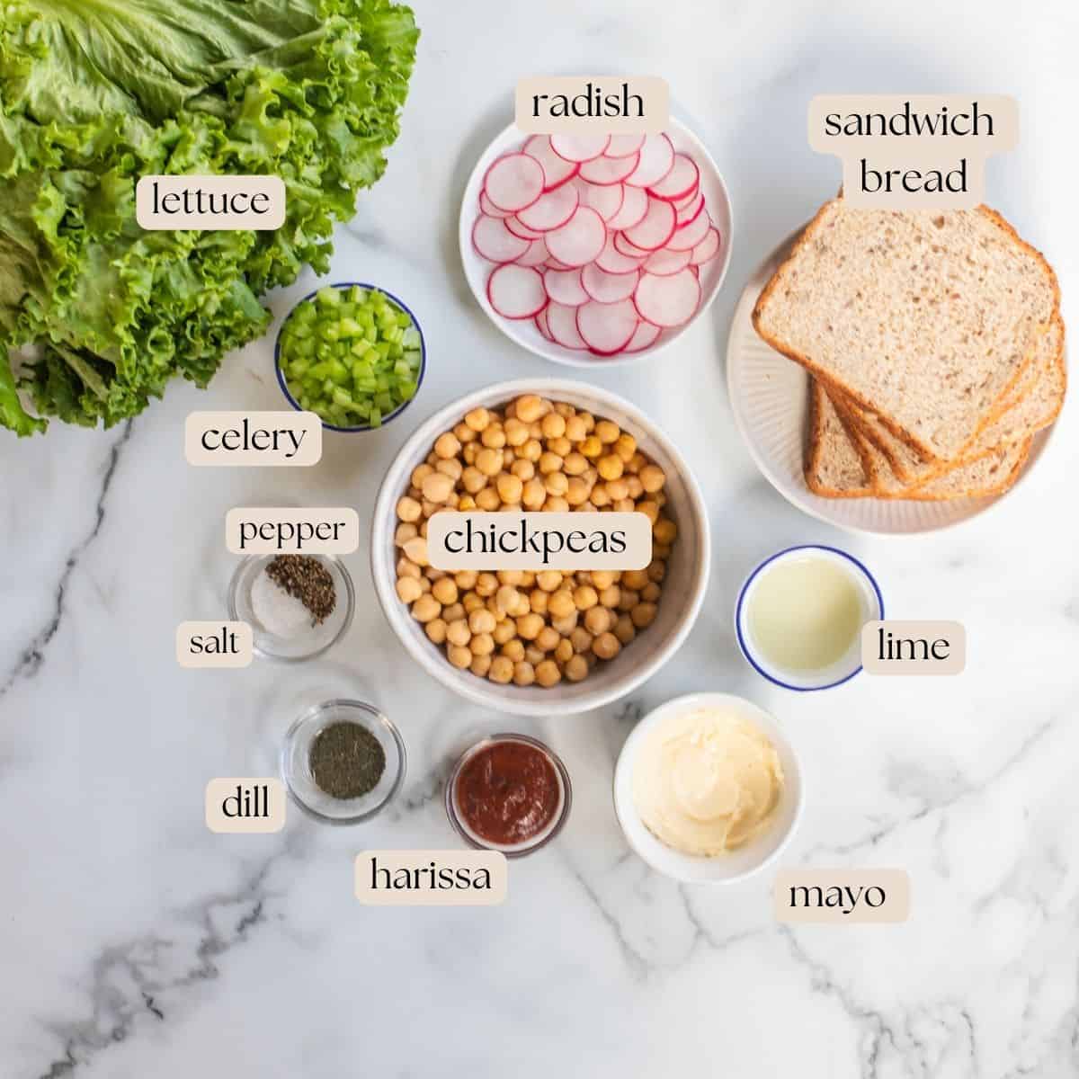 Ingredients to make smashed chickpea sandwich in bowls, plates and pinch bowls, including harissa.