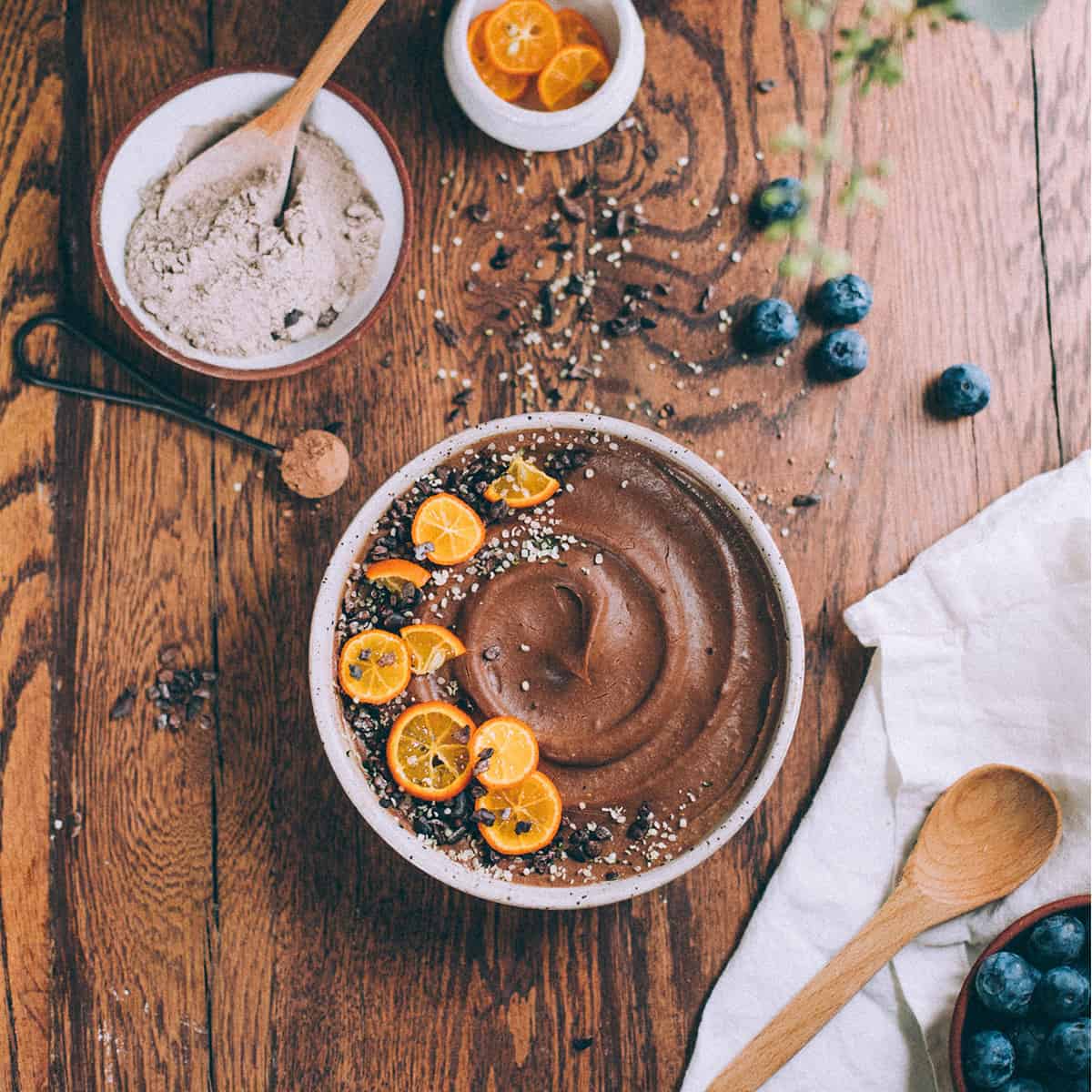 Chocolate teff porridge with orange slices placed on top on a staged wooden tabletop.