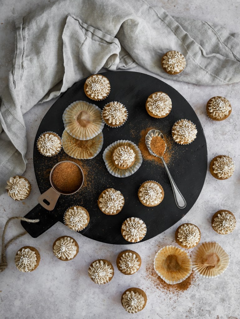 22 Coconut sugar cupcakes with fancy frosting on a staged tabletop.