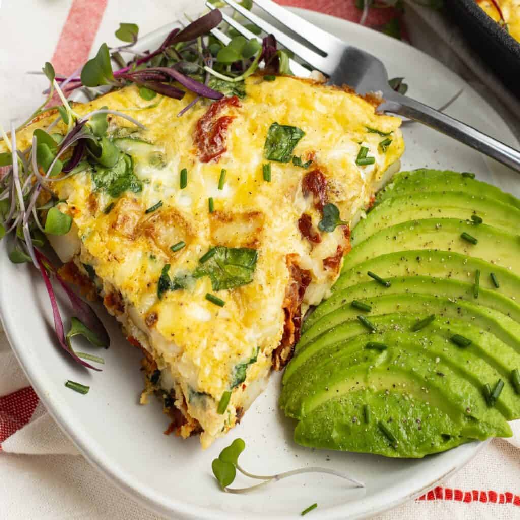 Cottage cheese frittata with salad and sliced avocado on a plate, showing fresh chopped chives on top.