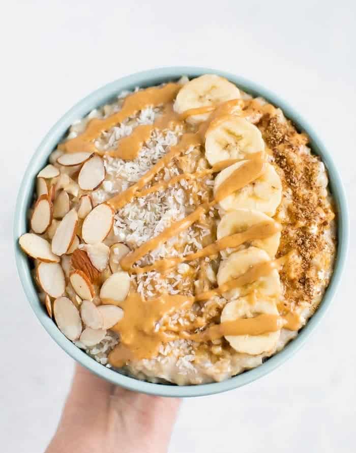 Cottage cheese oatmeal topped with sliced almonds, shredded coconut, banana and coconut sugar with a peanut butter drizzle.