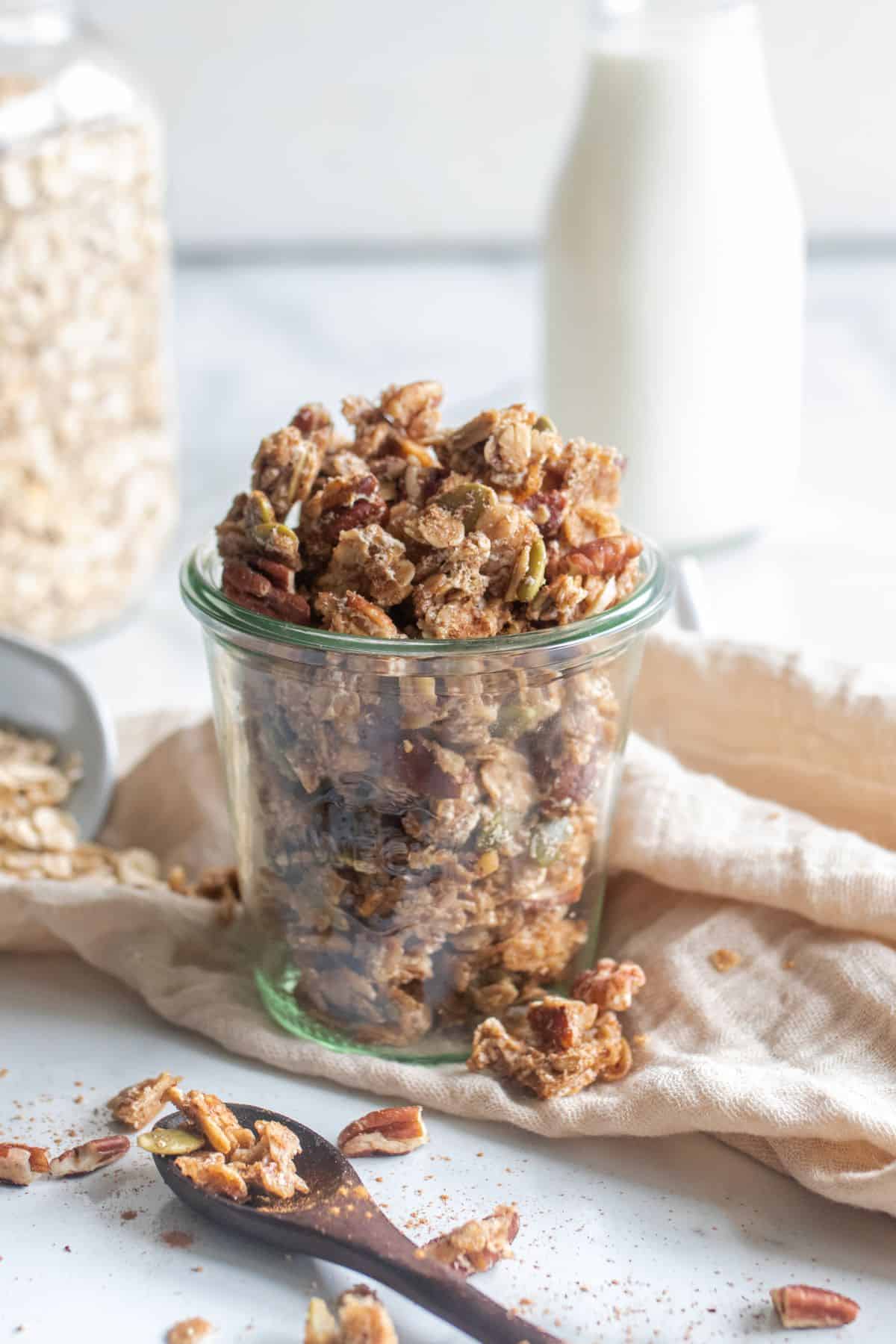 Egg white granola in a glass jar on a staged countertop with granola sprinkled around.