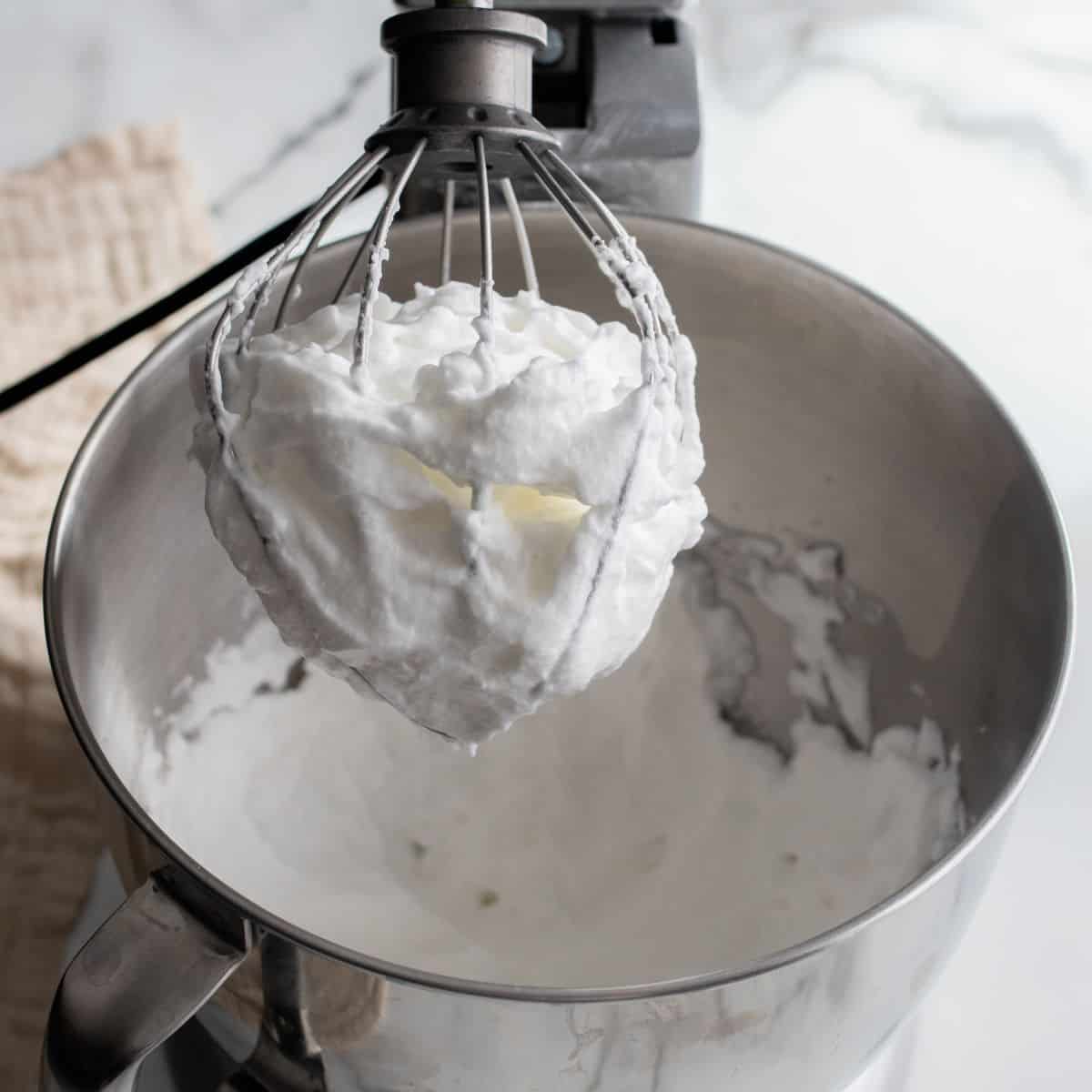 Egg whites on a wire whip showing properly forming peaks in a kitchen aid mixer.