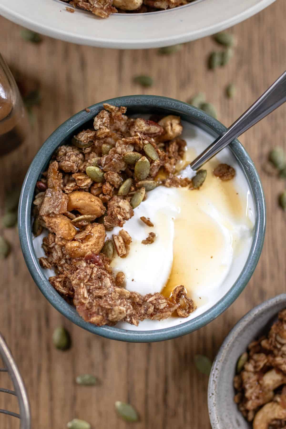 A bowl of yogurt with maple syrup and egg white granola on top with a spoon inside.