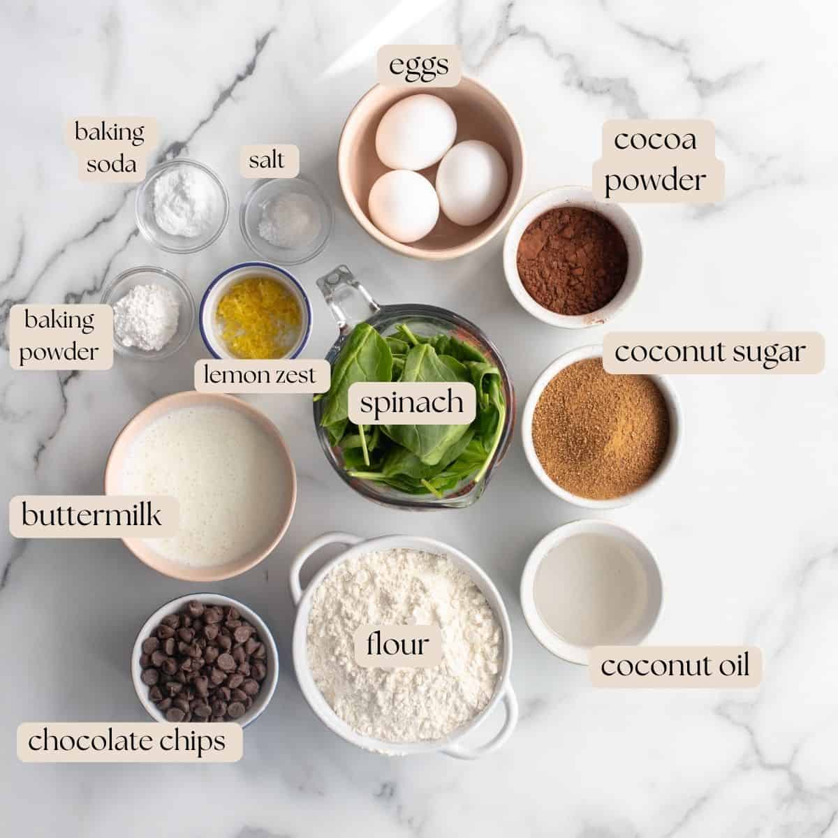 Ingredients to make green smoothie chocolate chip muffins in bowls and pinch bowls around a glass measuring cup full of spinach. 