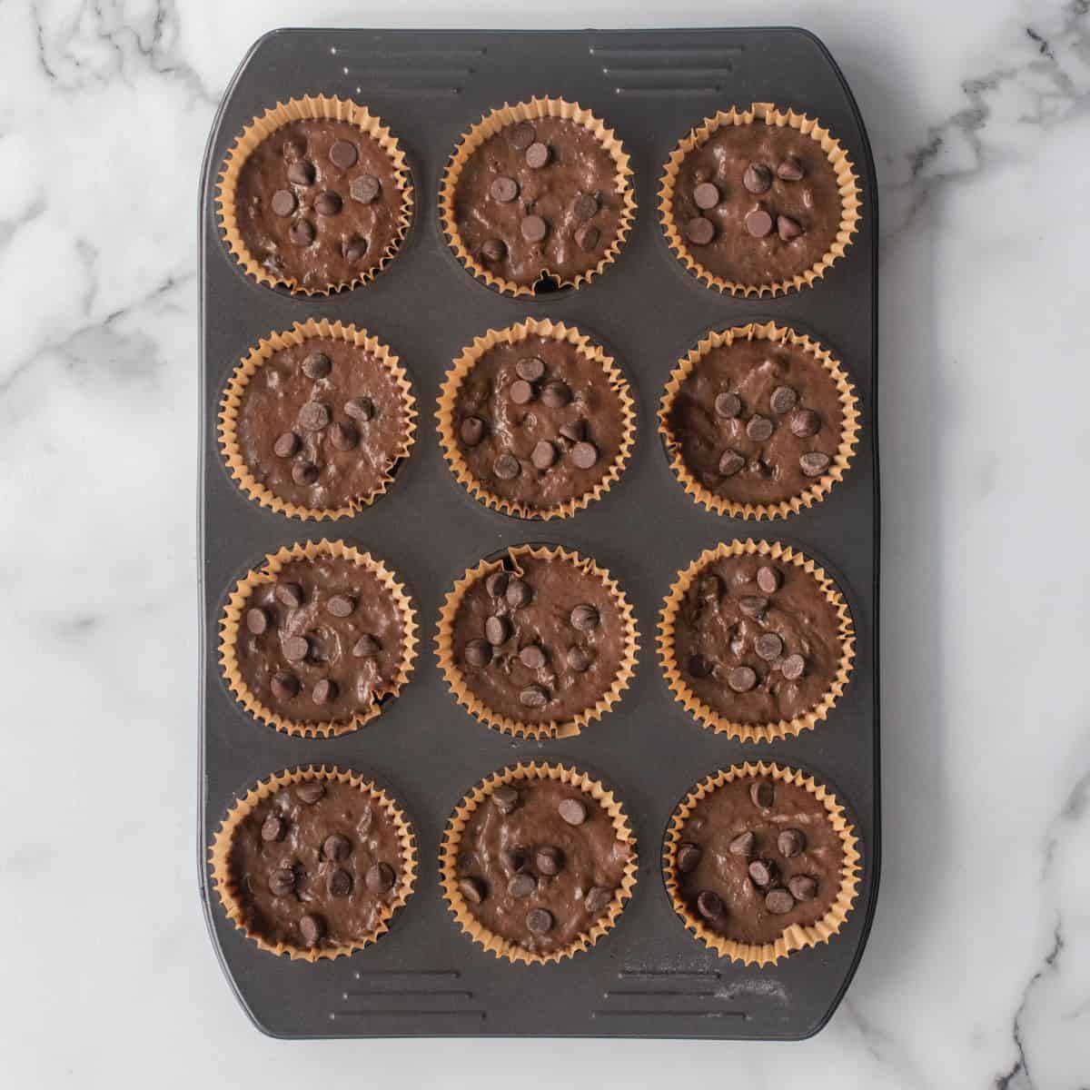 Muffin mixture in lined muffin tin with chocolate chips dropped on top of each one.