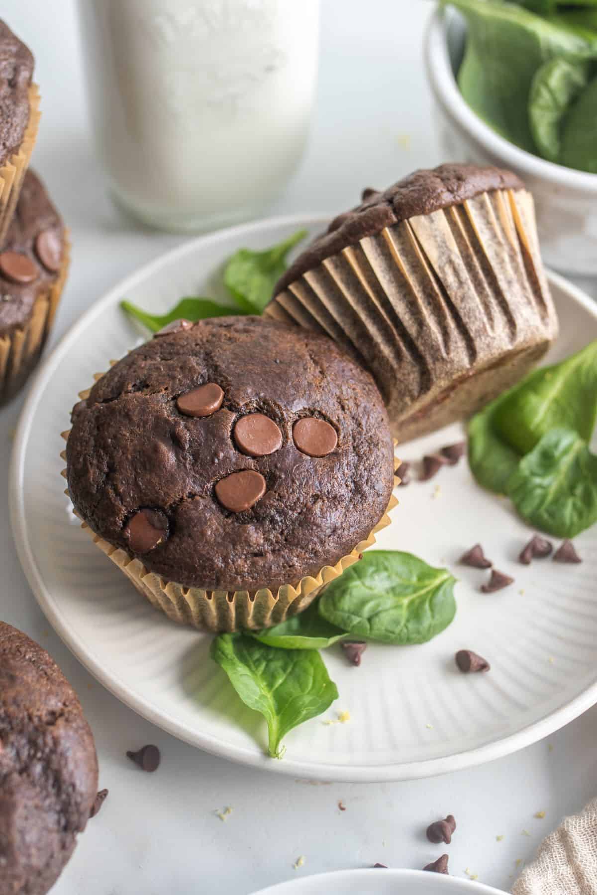 Two green smoothie chocolate muffins on a plate with spinach leaves around.