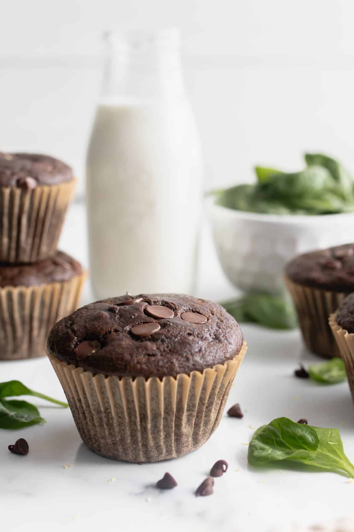 Green smoothie muffin on a staged counter top with muffins and spinach around.