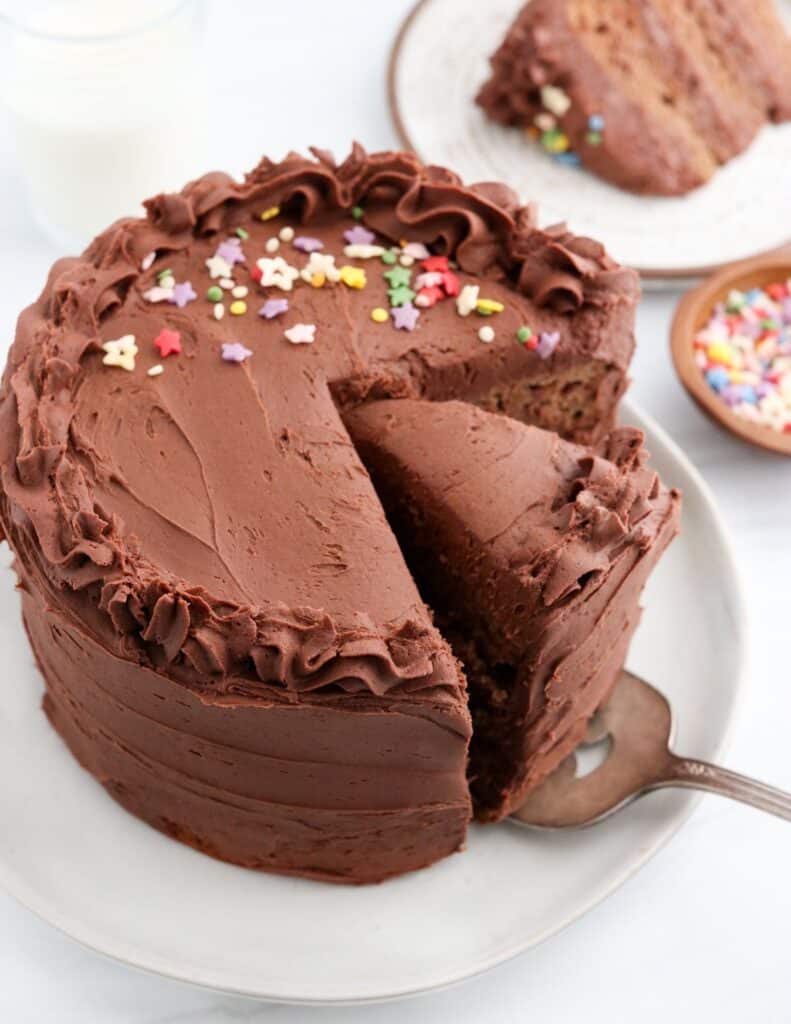 Piece of grain-free chocolate cake with chocolate icing being taking out by a cake server.
