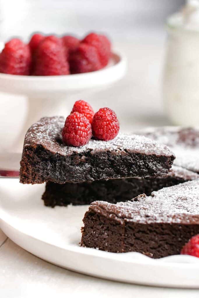 A close up of a piece of kladdkaka, also known as Swedish chocolate sticky cake, on a cake server with three raspberries on top.