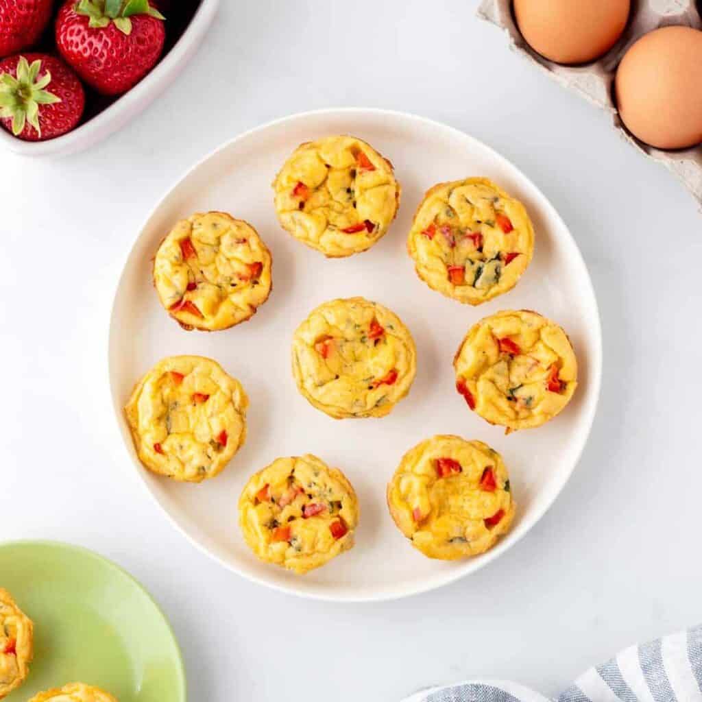 Mini, savory egg bites showing sliced bell peppers bits in them, on astaged plate.