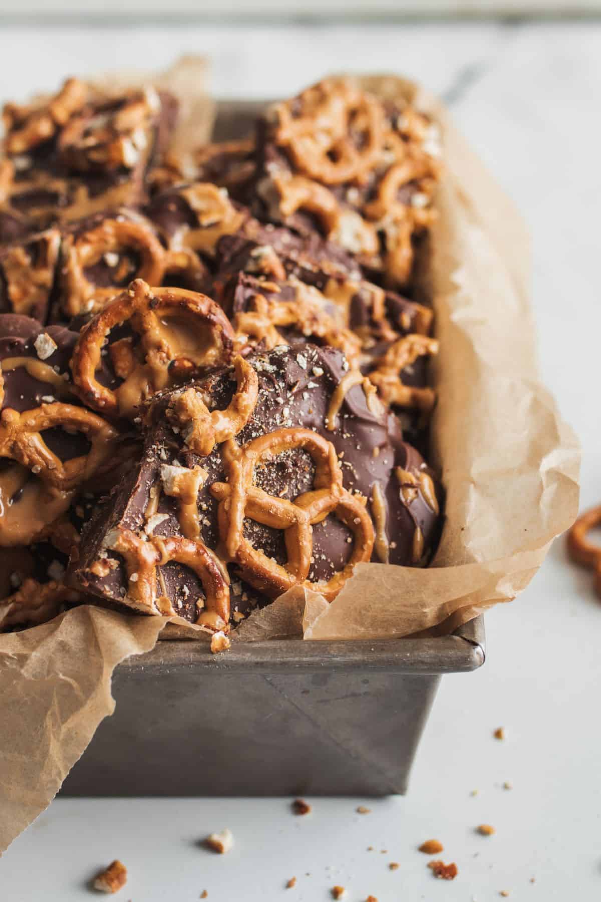 Date bark chopped and set in a parchment paper lined loaf pan, showing the texture of salt and pretzels on top of chocolaty date bark.