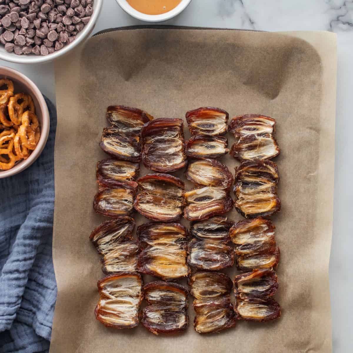 Date halves on parchment paper on a baking sheet on a staged countertop.