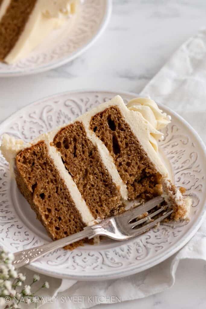 Triple layer vanilla cake on a white plate with a fork and bite missing.