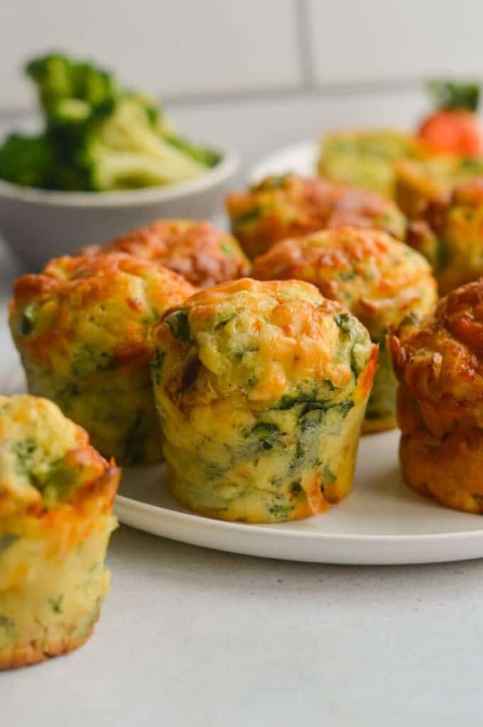 Mini, savory cottage cheese muffins on a serving plate with a bowl of broccoli behind them.