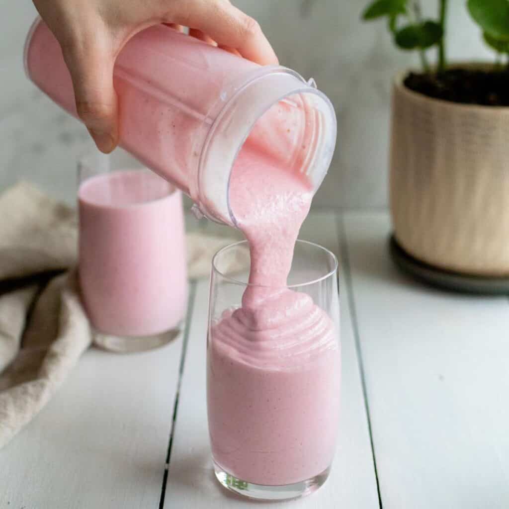 Strawberry cottage cheese smoothie pouring into a glass out of a blender cup on a staged tabletop.