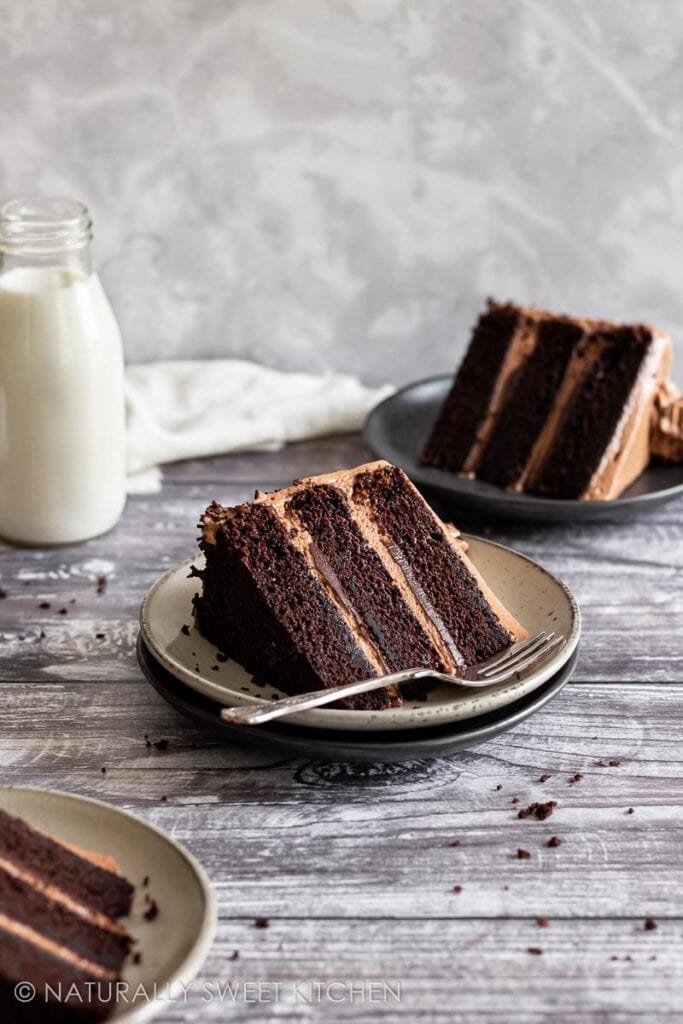 Three plated pieces of triple layer chocolate cake on a staged farmhouse wooden table.