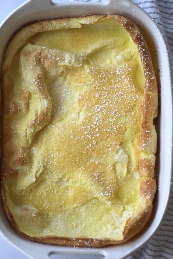 Large, German pancake in a casserole dish with sugar powdered on top.