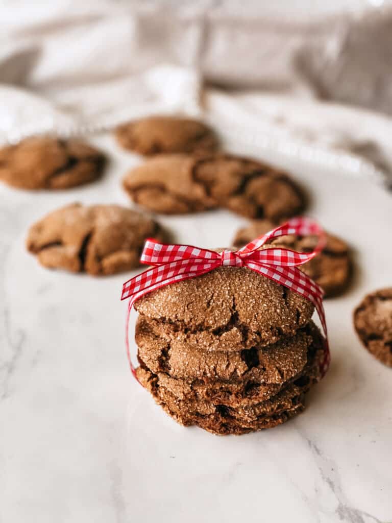 Four einkorn ginger cookies wrapped in a gingham bow with others behind them on a staged countertop.
