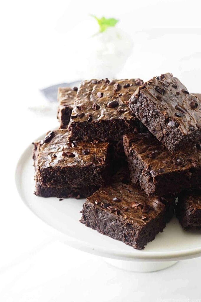 Chocolate brownies stacked on a plate, showing on the surface.