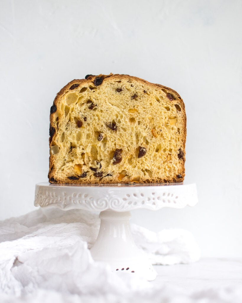 Half a loaf of einkorn panettone on an ornate , white, cake stand, showing the inside texture with small air pockets.