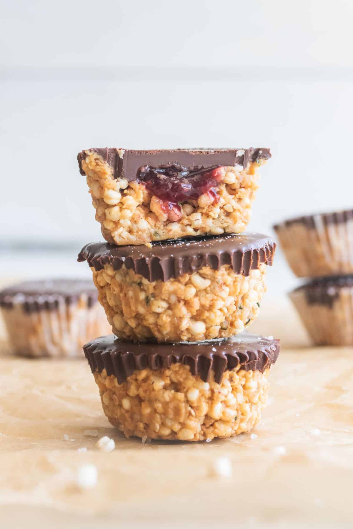 Three quinoa bites stacked on top of each other on a parchment paper with others staged around with a bite out of the top one showing raspberry jam inside.