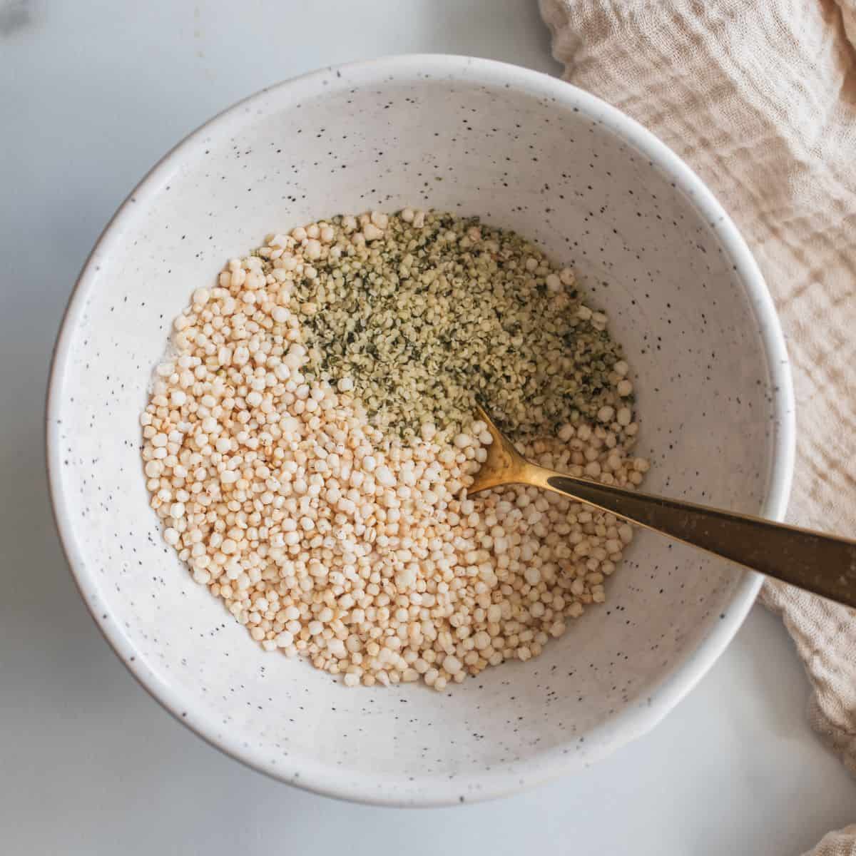 Puffed quinoa, hemp hearts and salt in a ceramic bowl with a spoon inside ready to mix together.
