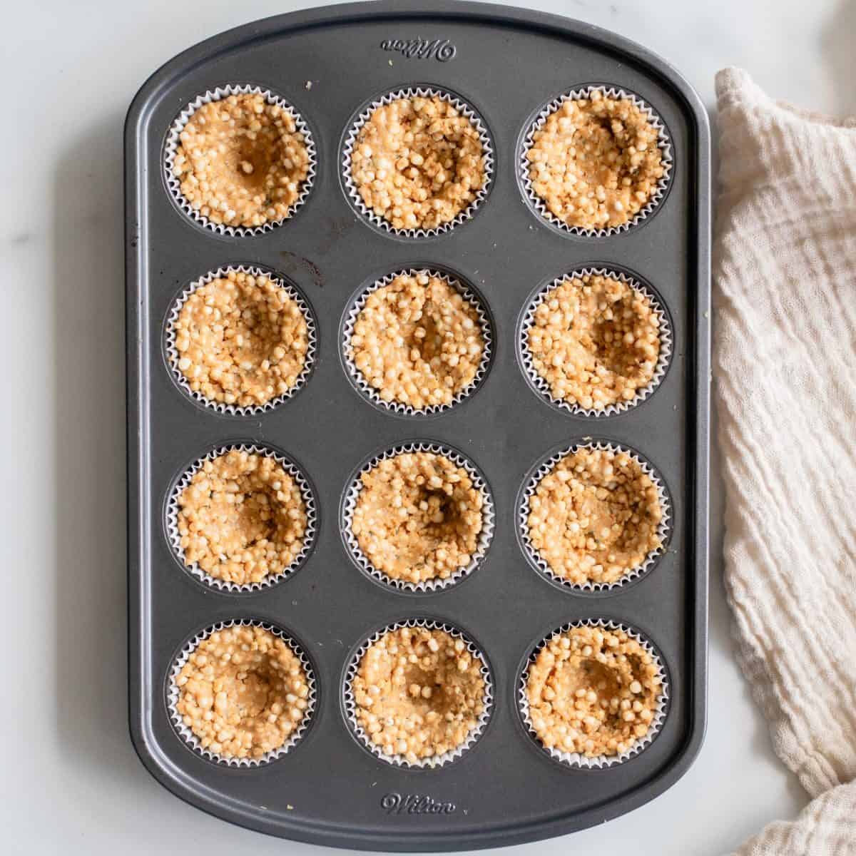 Puffed quinoa mixture pressed into lined muffin tin.