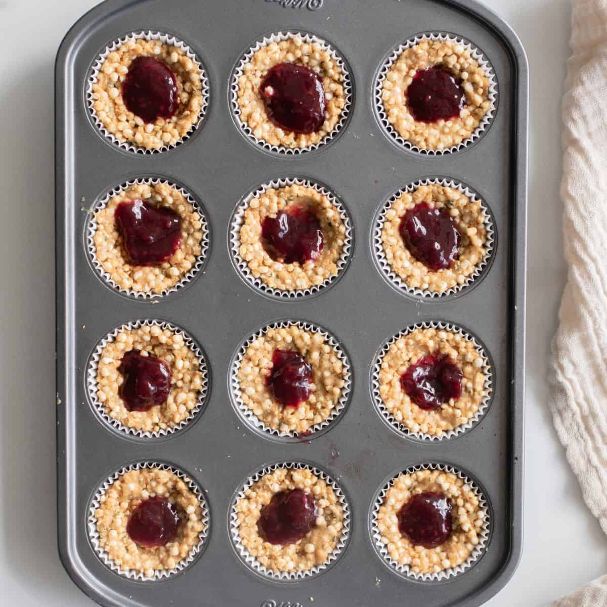 Mixed berry jam dropped on top of puffed quinoa mixture pressed into lined muffin tin.