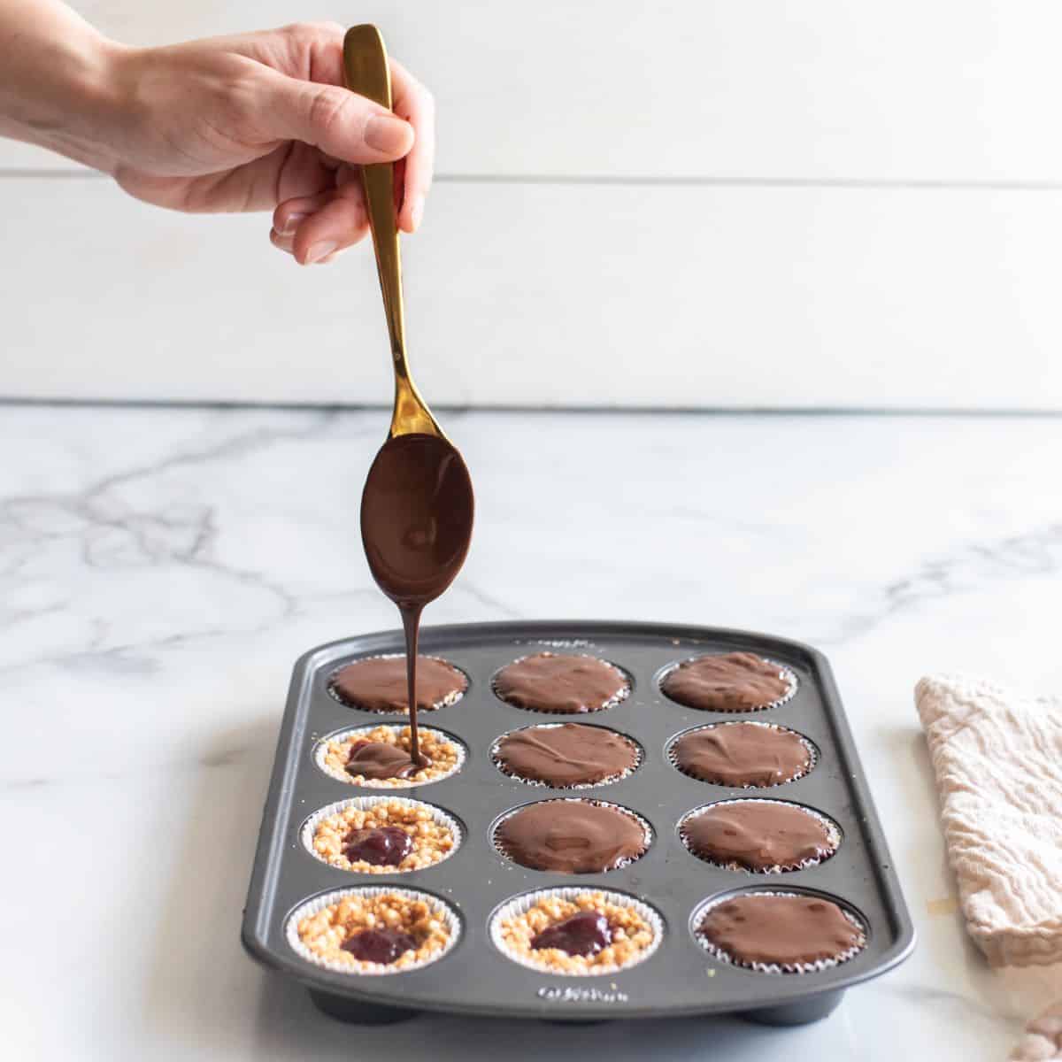 Melted chocolate pouring over quinoa bites mixture in a lined muffin tin.