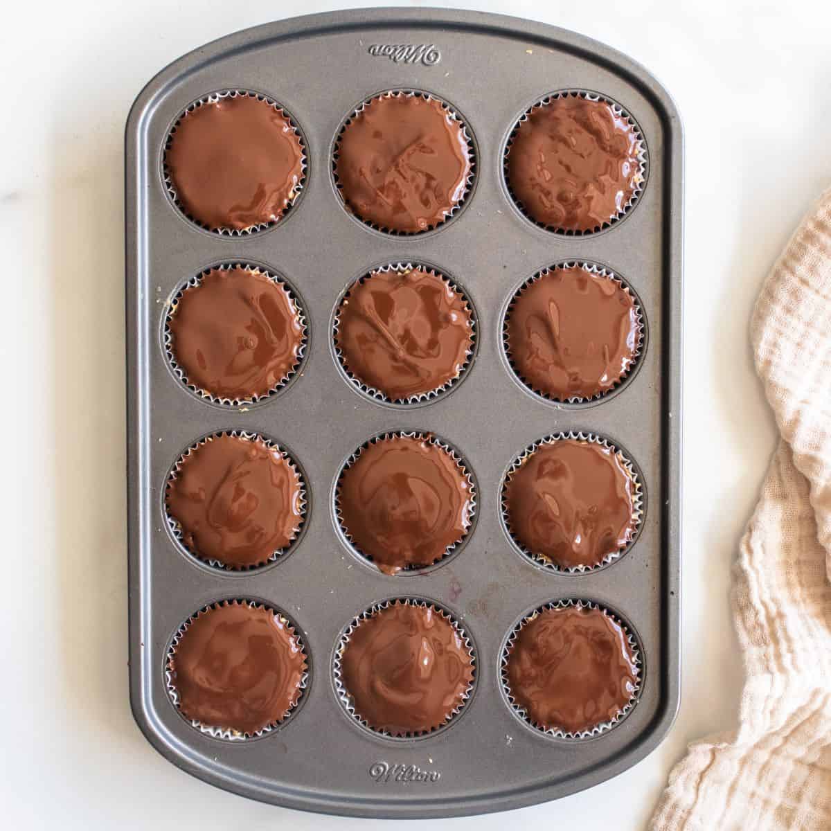 Overhead view of quinoa bites in a lined muffin tin setting on a countertop showing glinting melted chocolate.
